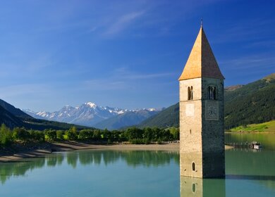 Reschensee mit Kirchturm bei Sonennschein mit Bergpanorama | © Gettyimages.com/LianeM