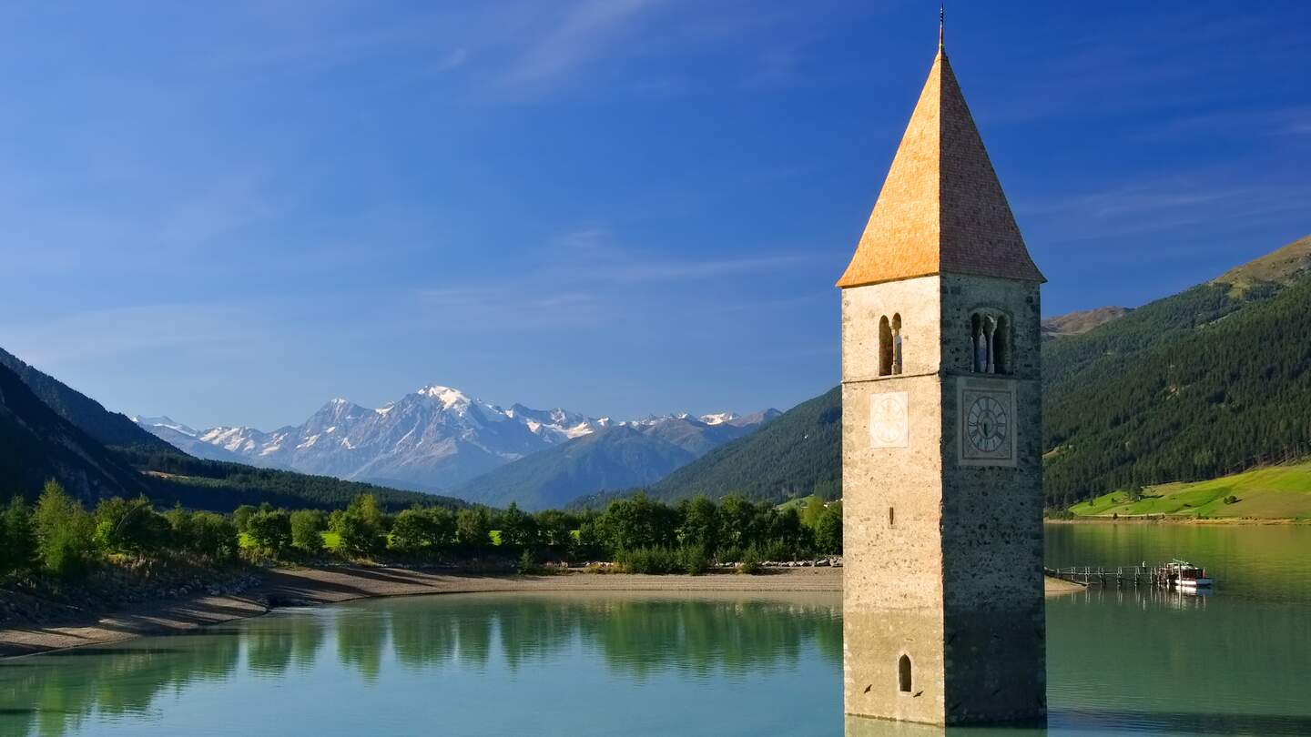 Reschensee mit Kirchturm bei Sonennschein mit Bergpanorama | © Gettyimages.com/LianeM