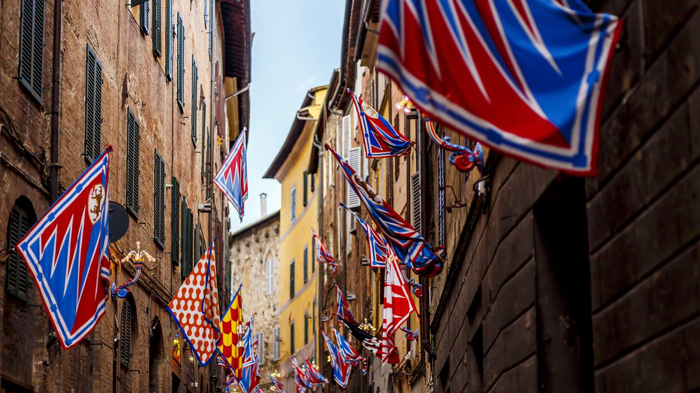 Flaggen der Kontrahenten des jährlichen Pferderennens Palio de Siena in der Innenstadt von Siena | © Gettyimages.com/SimoneN