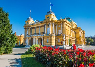 Blick auf das Nationaltheater in Zagreb, Kroatien bei blauem Himmel und Blumen im Vordergrund | © gettyimages.com/iascic