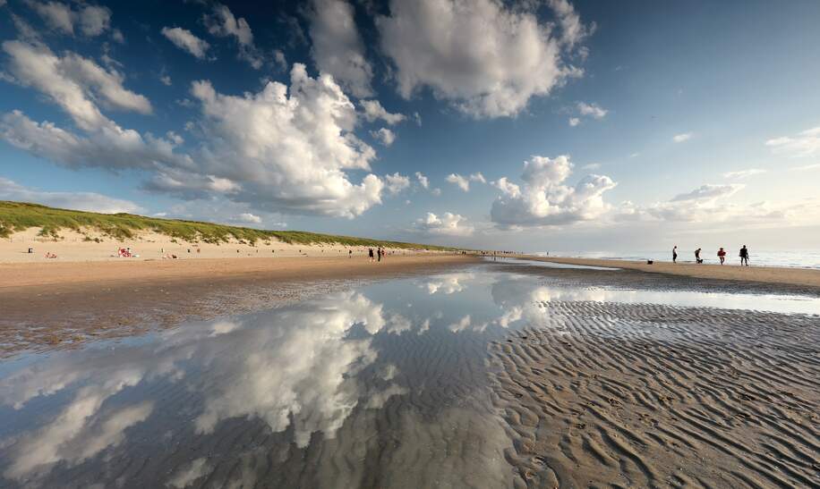 Der Himmel spiegelt sich in der letzten Pfuetze die die Ebbe uebrig gelassen hat Menschen spazieren ueber den Strand | © Gettyimages.com/olharohulya