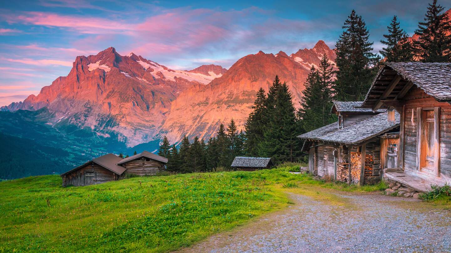 Bergkulisse, di im sonnenuntergang rot glüht, rechts ist eine Almhütte | © Gettyimages.com/Janoka82