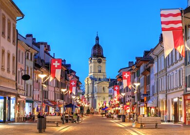 Nächtliche Szene entlang der Grand Rue in Morges, Schweiz, mit der Saint-Louis-Kirche im Hintergrund. | © Bogdan Lazar