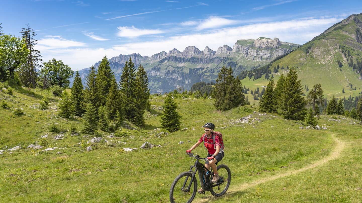 Fahrradfahrerein fährt bergauf inmitten der Schweizer Alpen bei Sonnenschein und leichten Wolken | © Gettyimages.com/Uwe Moser