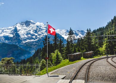 Die Flagge der Schweiz flattert mit der Eisenbahn und dem Berg Jungfrau im Hintergrund. | © gettyimages.com/possawat