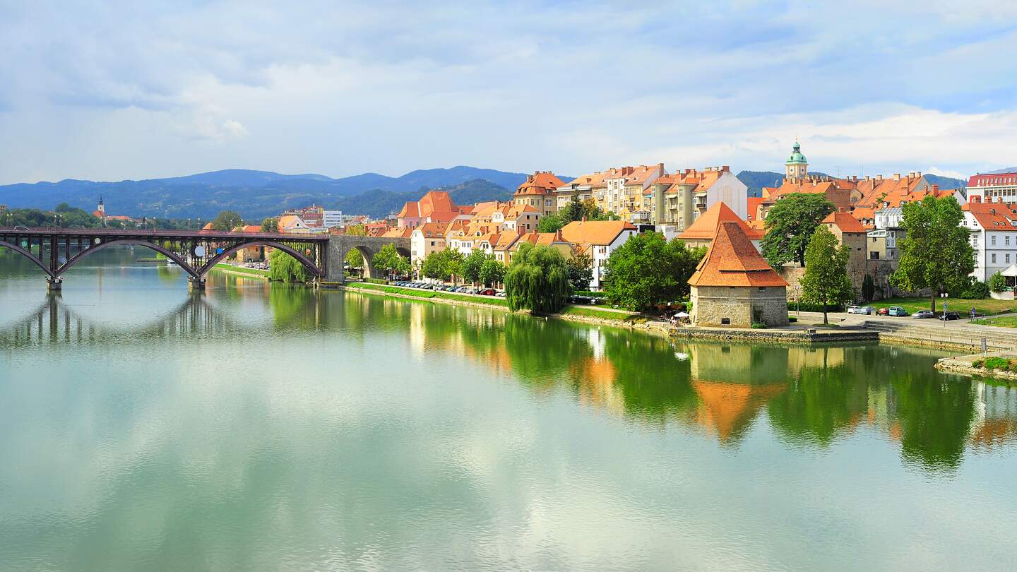 Blick auf einen Fluss mit einer Brücke und im Hintergrund sieht man Häuser der Stadt Maribor in Slowenien | © Gettyimages.com/joyt