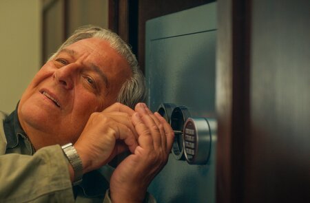 Der Schauspieler Christian Clavier knackt ein Schloss in einer Szene des Kinofilms "Ab durch die Mitte – Mit Vollgas durch Paris" | © Happy Entertainment