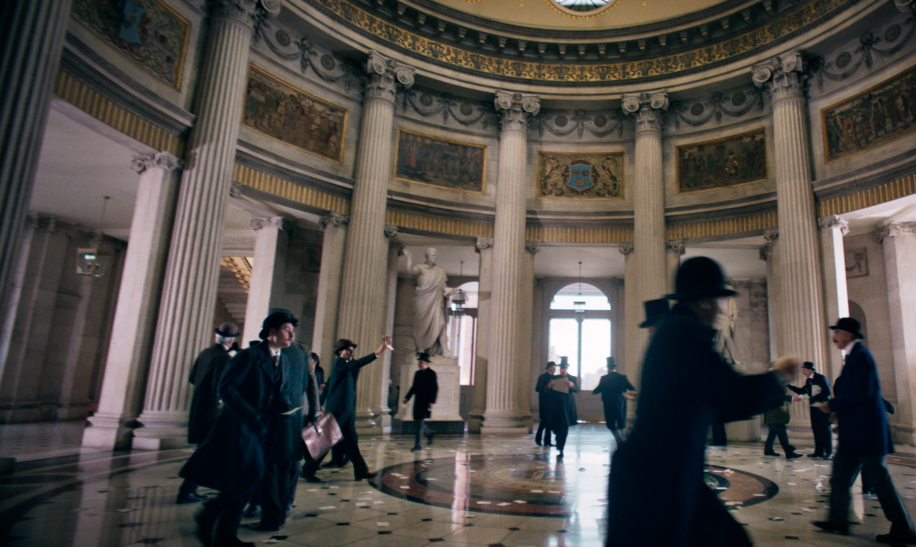 Eine große, monumentale Rotunde mit hoher Kuppel und aufwendig verziertem Gesims. Mehrere hohe, gerillte Säulen aus hellem Stein umgeben den runden Raum. Zwischen den Säulen befinden sich reich verzierte Wandfriese und Mosaike. Im Zentrum steht eine große Statue auf einem Podest. Auf dem glänzenden Marmorboden sind kreisförmige Muster zu erkennen. Mehrere Personen in historisch wirkender Kleidung bewegen sich durch den Raum. | © polyband/Palatin Media/Albion Television Ltd