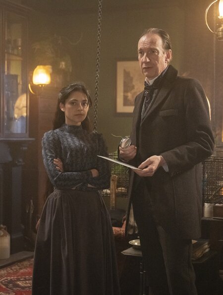 Die Figuren Sherlock Holmes und Amelia Rojas aus der Serie "Sherlock & Daughter" stehen in einem dunklen altmodischen Raum | © polyband/Palatin Media/Albion Television Ltd