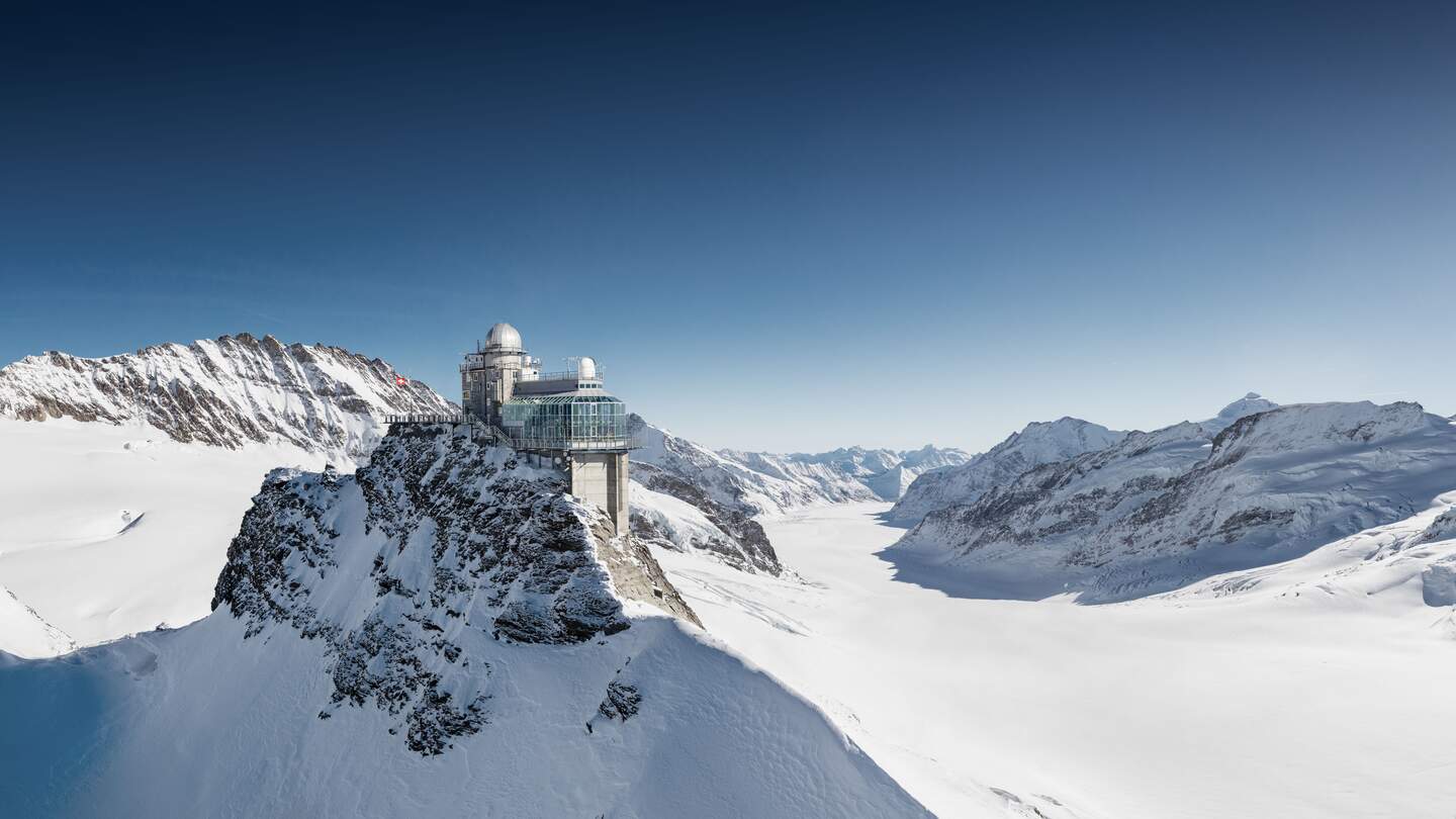 Jungfraujoch  | © Jungfraubahnen Hochgelegenes Gebäude auf einem verschneiten Berggipfel mit Kuppelbau. Umgeben von schneebedeckten, zerklüfteten Berglandschaften unter klarem, blauem Himmel. | © Jungfraubahnen