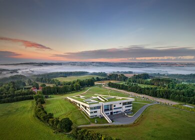 Luftaufnahme des Moesgaard Museums bei Aarhus, eingebettet in eine weitläufige Landschaft mit Wäldern und Nebelschwaden.  Geben Sie Ihr Feedback zu BizChat ab. | © Foto Medieafdelingen Moesgaard Museum