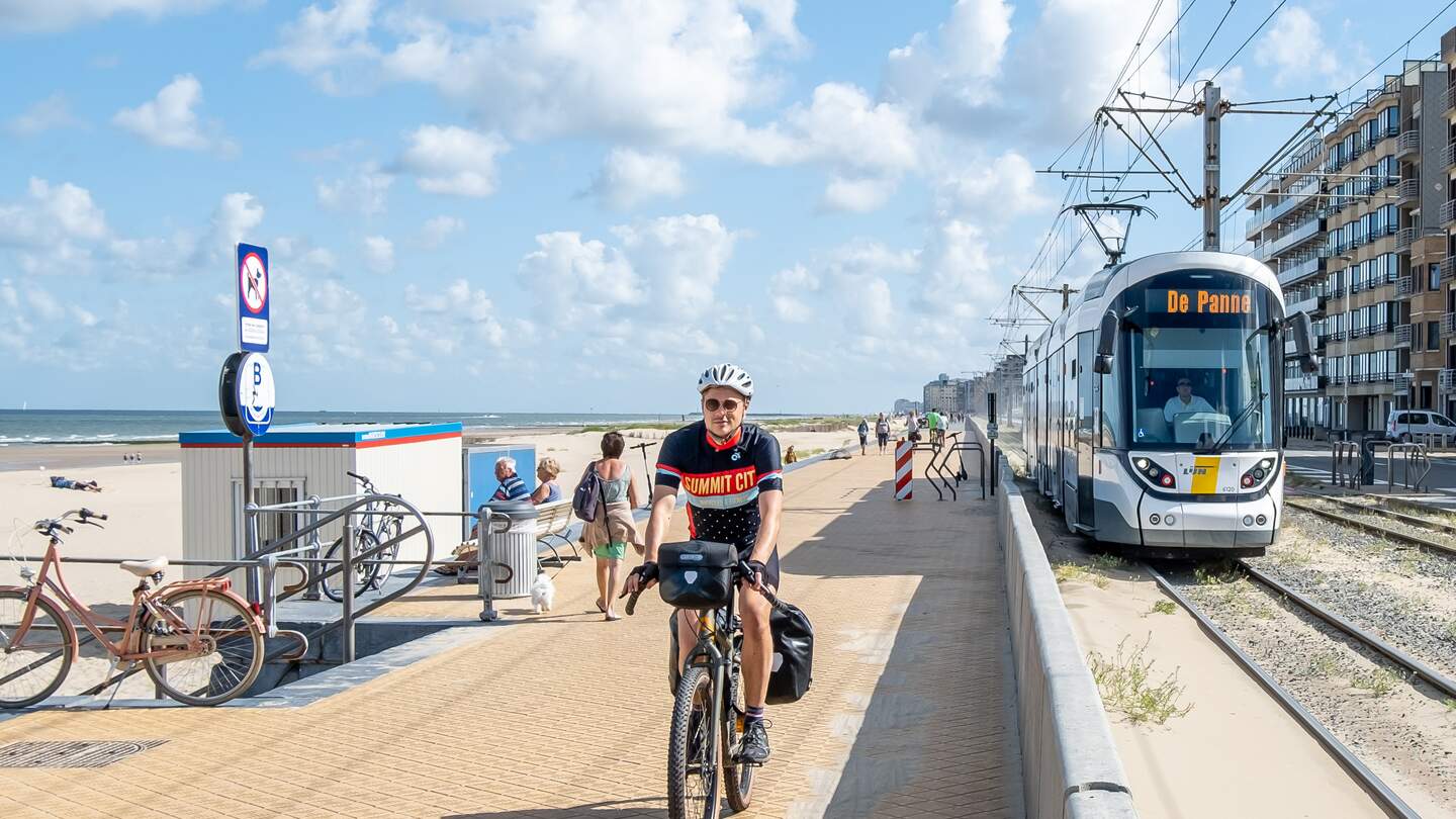 Radfahrer an der Küste von Belgien mit der Straßenbahn Kusttram im Hintergrund auf der Strecke Oostende nach Diskmuide | ©  Bas van Oort