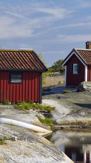 Drei rote Holzhütten mit weißen Fensterrahmen stehen auf Felsen am Wasser. | © imagebank.sweden.se/Ola Ericson