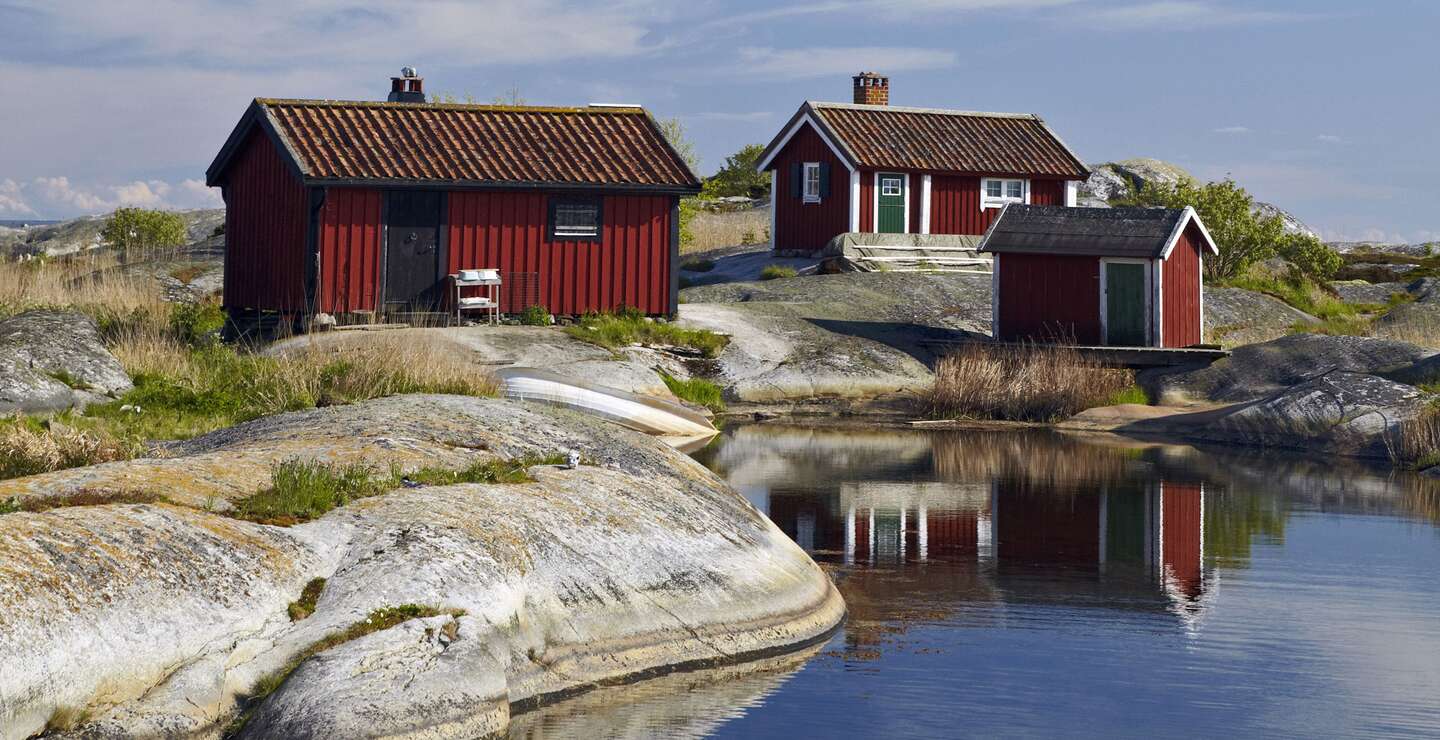 Drei rote Holzhütten mit weißen Fensterrahmen stehen auf Felsen am Wasser. | © imagebank.sweden.se/Ola Ericson