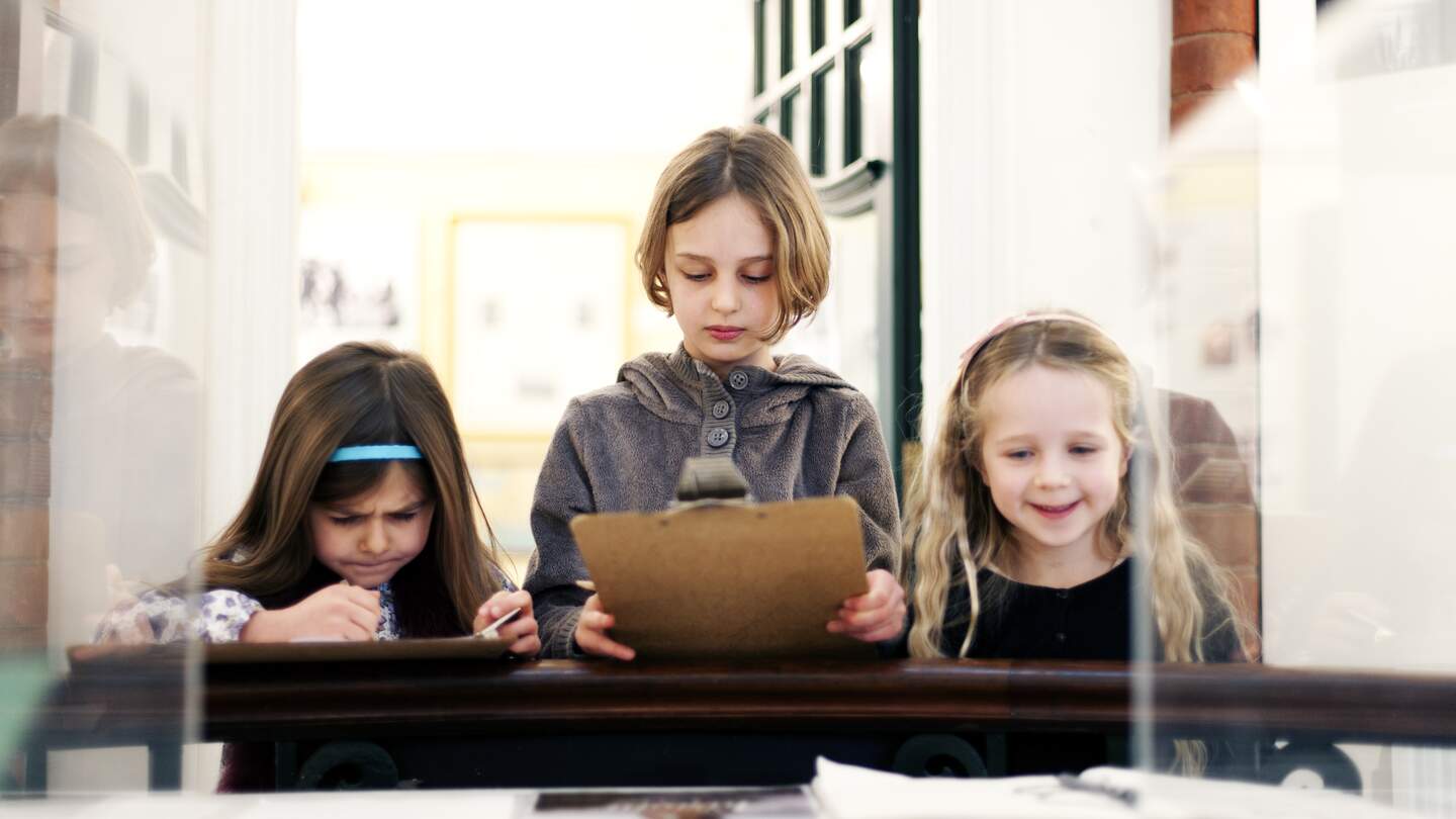 Drei Kinder in einer Museums Ausstellung stehen vor einem Glaskasten. | © Gettyimages.com/Rene Mansi