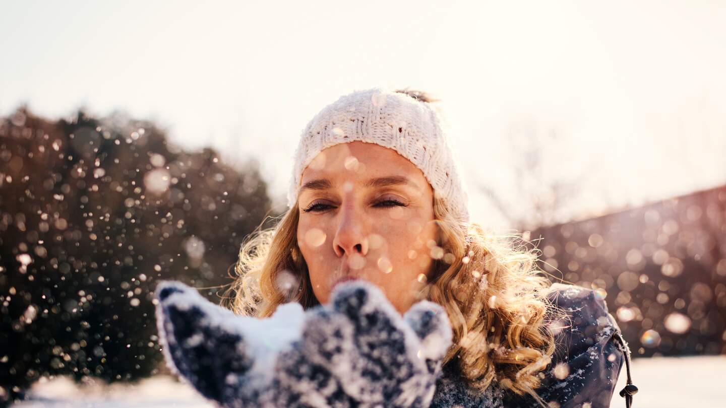 Erwachsene Frau, im Winter draussen, Schnee pustend | © © Gettyimages.com/vgajic