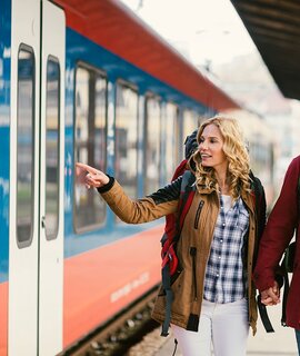 Mitte erwachsenes Paar Rucksacktouristen am Bahnhof. Sie tragen Rucksaecke und Karte. Am Bahnhof auf den Zug warten und Haendchen halten | © Gettyimages.com/vgajic