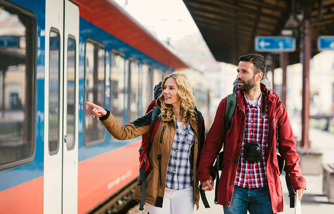Mitte erwachsenes Paar Rucksacktouristen am Bahnhof. Sie tragen Rucksaecke und Karte. Am Bahnhof auf den Zug warten und Haendchen halten | © Gettyimages.com/vgajic