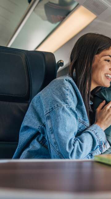 Pärchen im Zug an einem Tisch schauen auf ein Handy | © GettyImages.com/miloradkravic