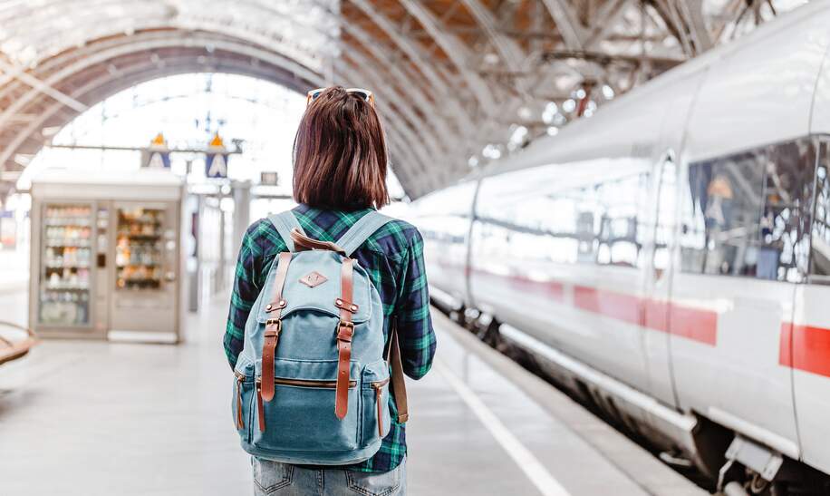 Frau mit Rucksack beobachtet einen Zug am Bahnhof | © GettyImages.com/frantic00