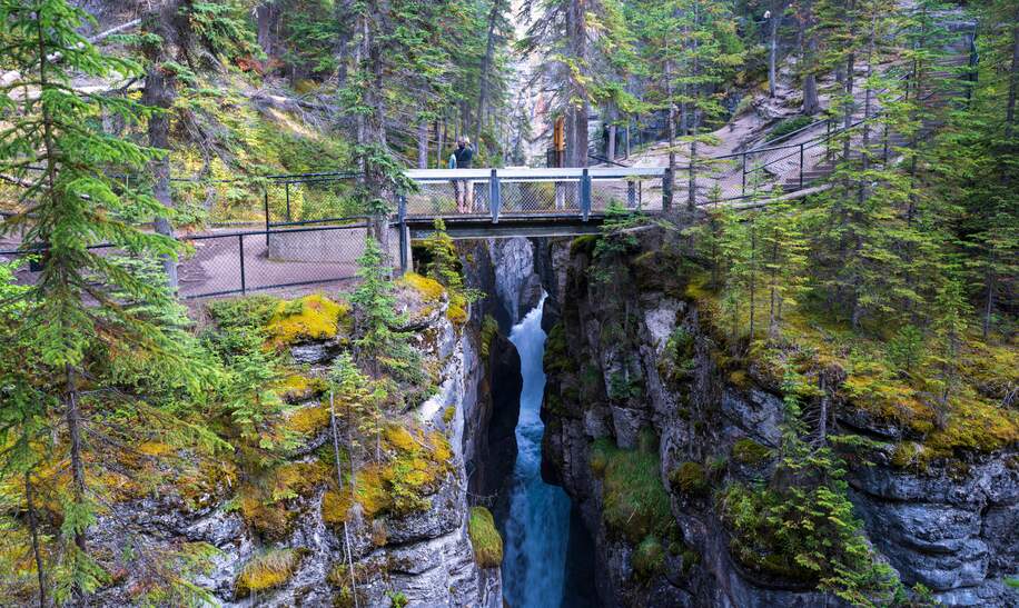 Blick auf den Maligne Canyon in Alberta, eine Touristin steht auf einer Brücke und schießt Fotos.  | ©  Gettyimages.com/redtea