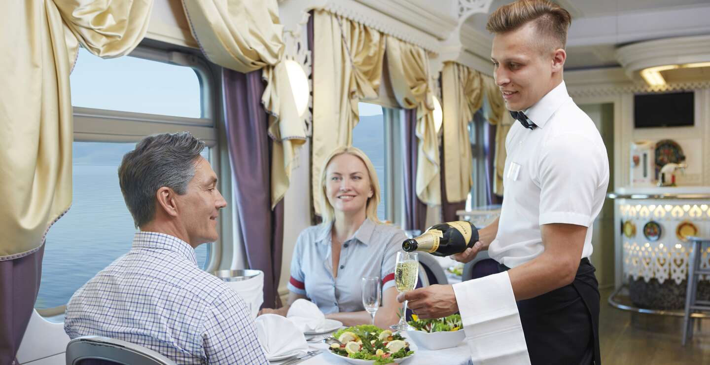 Ein Mitarbeiter bedient zwei Passagiere im Restaurant in der Zarengoldbahn | © Ross Hillier