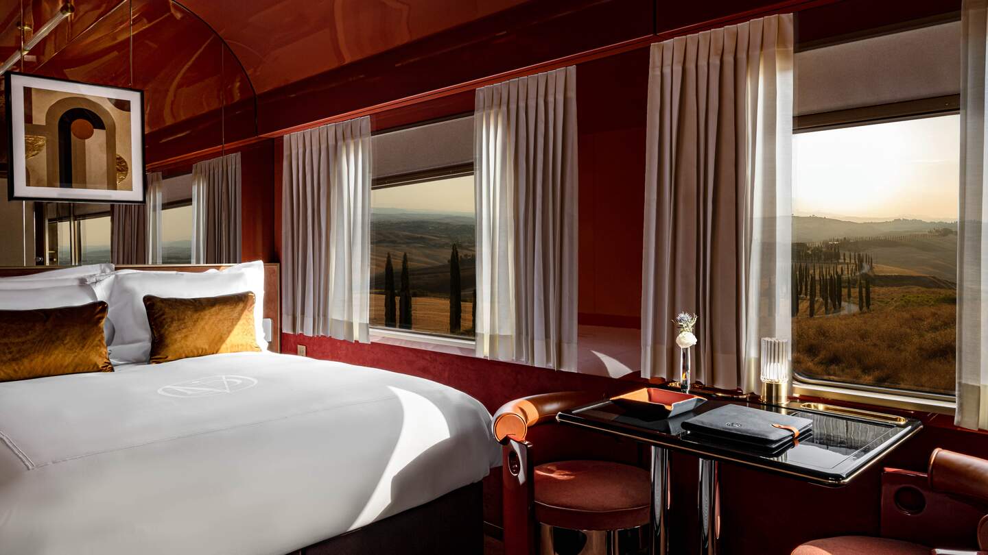 Blieck in die Suite des La Dolce Vita Orient Express mit großen Panoramafenstern, einem Doppelbett auf der linken Seite, und einem Tisch mit zwei Stühlen in der Mitte | © Orient Express SAS