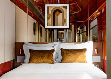 Blick in die Suite des La Dolce Vita Express mit Doppelbett im Vordergrund auf der linken Site ein kleines gemütliches Sofa | © Orient Express SAS