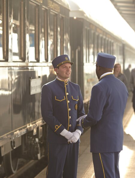 Stewards stehen auf dem Bahnsteig vor dem Venice Simplon Orient Express. Passagiere laufen vorbei. | © © Matt Hind