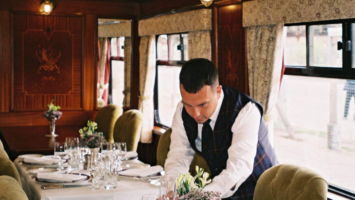 Luxuriöser Speisewagen mit elegant gedecktem Tisch. Ein Kellner richtet den Tisch her | © belmond.com/The World from a Window