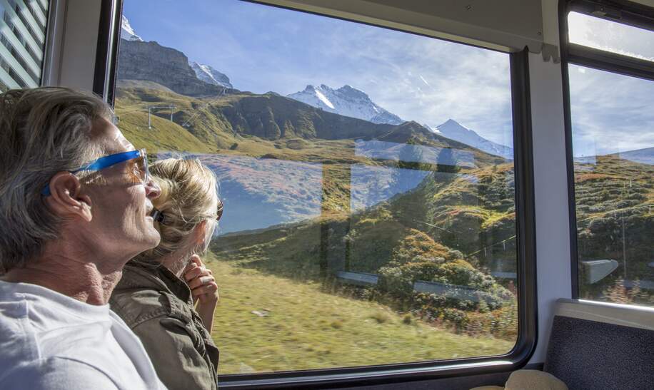 Bestager-Paar genießt den Blick aus einem Zugfenster, auf das sonnige Panorama der Schweizer Berge | © Gettyimages/AscentXmedia