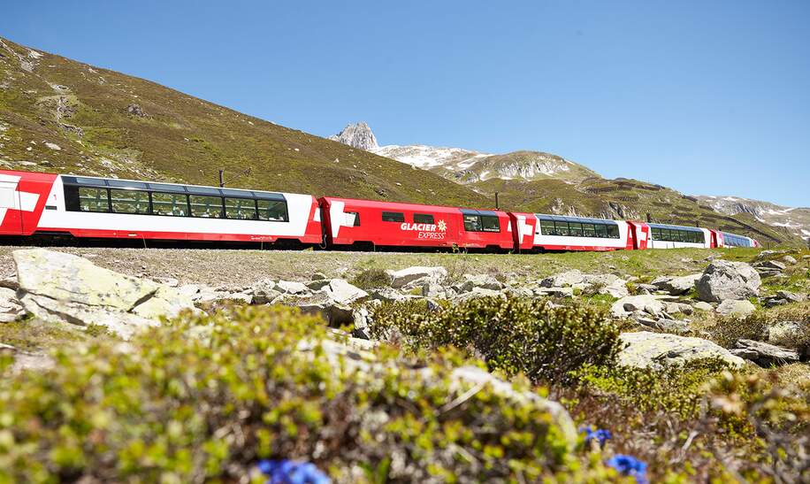 Der Glacier Express fährt über den Oberalppass in den Schweizer Alpen im Frühling | © Glacier Express AG/Stefan Schlumpf