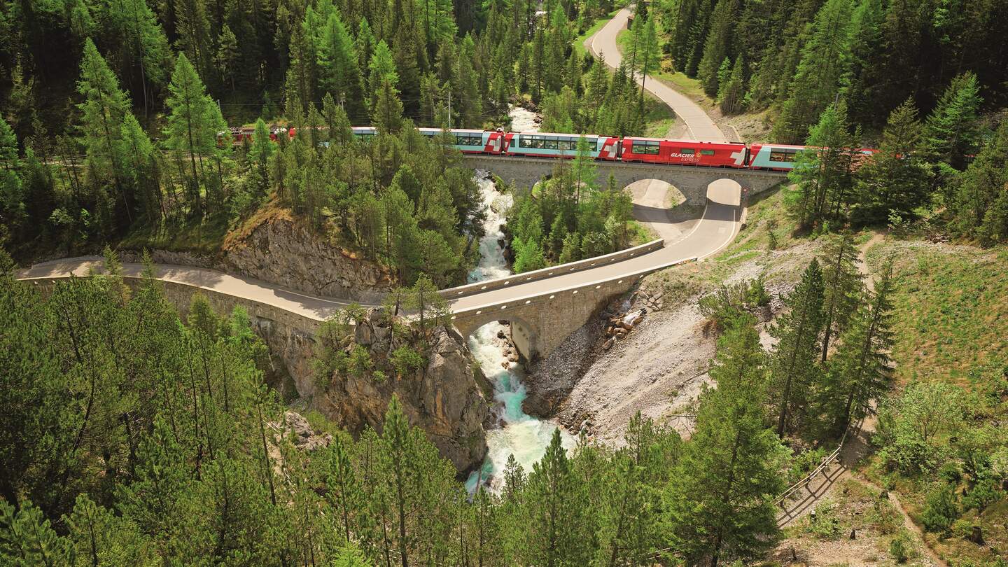 Glacier Express fährt über eine Brücke umringt von dichtem Wald | © Rhätische Bahn/Stefan Schlumpf