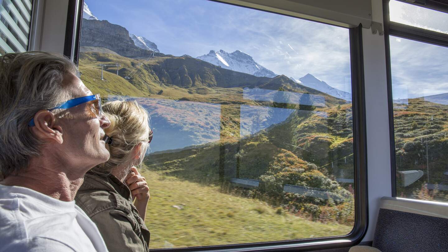 Bestager-Paar genießt den Blick, aus einem Zugfenster, auf das sonnige Panorama der Schweizer Berge | © © Gettyimages/AscentXmedia