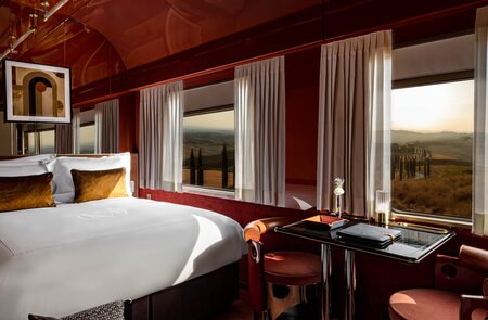 Blieck in die Suite des La Dolce Vita Orient Express mit großen Panoramafenstern, einem Doppelbett auf der linken Seite, und einem Tisch mit zwei Stühlen in der Mitte | © Orient Express SAS