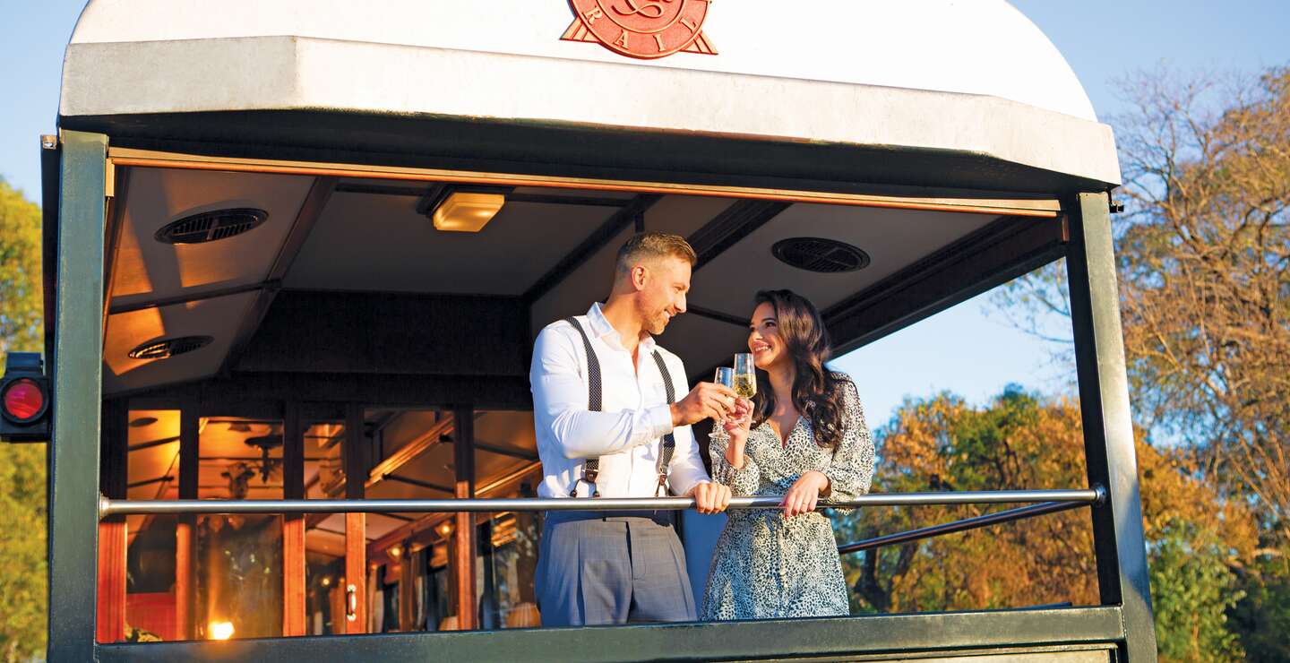 Paar steht auf dem Zug-Balkon des Luxuszuges Rovos Rail | © Rovos Rail Tours