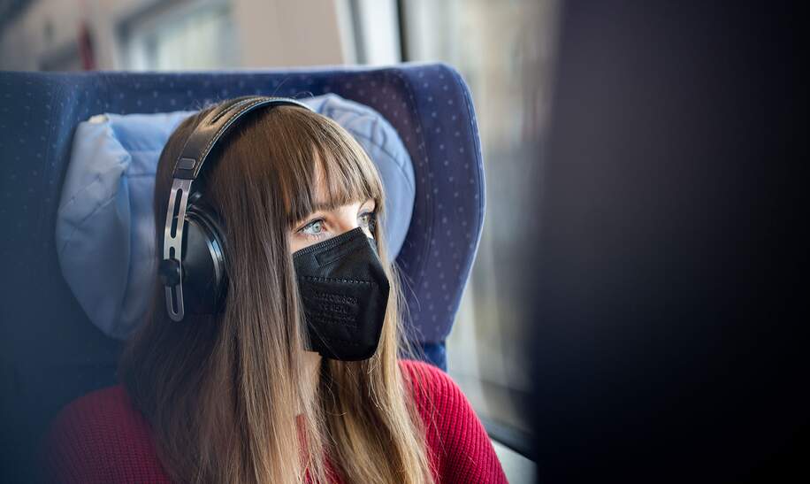 Eine Frau trägt eine schwarze Maske und Kopfhörer und blickt aus dem Fenster | © Deutsche Bahn AG/Patrick Kuschfeld
