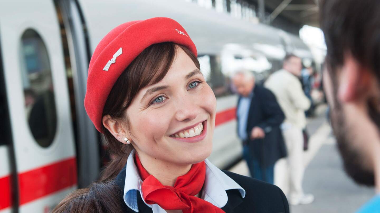Ein DB Mitarbeiter mit roter Mütze und Schal hilft einem Reisenden auf dem Bahnsteig mit seinem mobilen Gerät. | © Deutsche Bahn AG