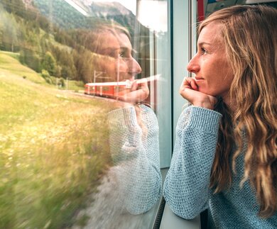 Frau, die mit dem Zug aus dem Fenster schaut und die landschaftlich vorbeifahrende Landschaft geniesst | © Gettyimages.com/Mystockimgaes