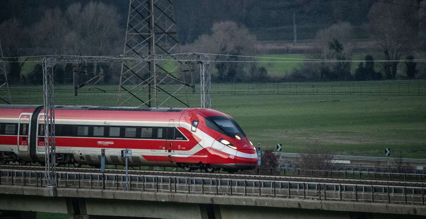 Ein rot-weißer Frecciarossa Zug fährt auf einer Brücke. Neben ihm ist eine Landschaft mit Bäumen zu sehen. | © Trenitalia