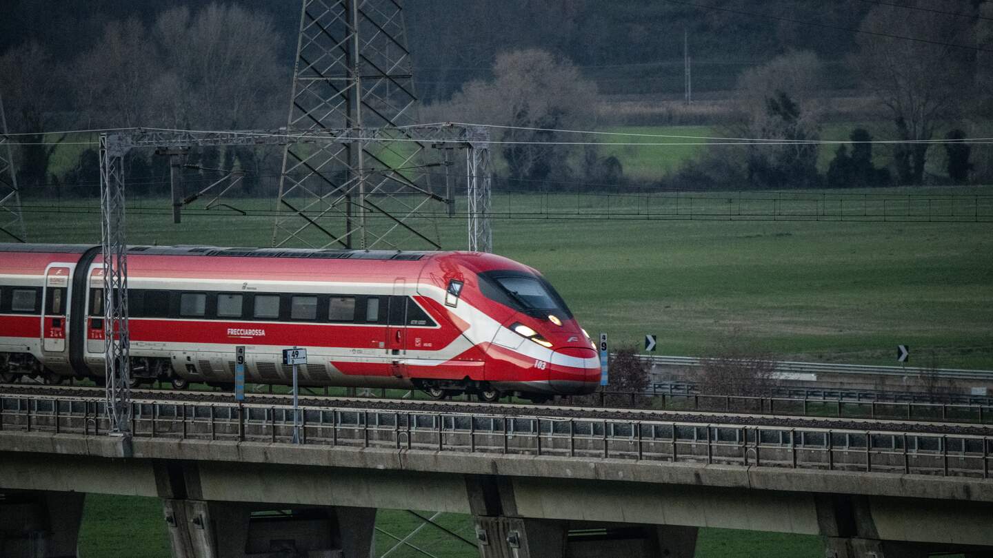 Ein rot-weißer Frecciarossa Zug fährt auf einer Brücke. Neben ihm ist eine Landschaft mit Bäumen zu sehen. | © Trenitalia