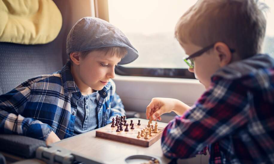 Zwei kleine Jungs, die die Bahnfahrt genießen und Schach spielen | © © Gettyimages.com/Imgorthand Zwei kleine Jungs, die die Bahnfahrt genießen und Schach spielen | © © Gettyimages.com/Imgorthand