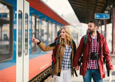Mitte erwachsenes Paar Rucksacktouristen am Bahnhof. Sie tragen Rucksaecke und Karte. Am Bahnhof auf den Zug warten und Haendchen halten | © Gettyimages.com/vgajic