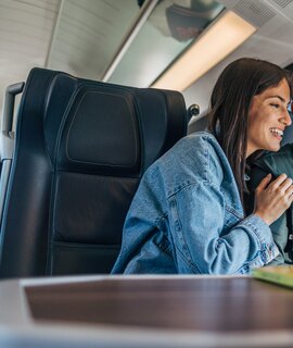 Pärchen im Zug an einem Tisch schauen auf ein Handy | © GettyImages.com/miloradkravic