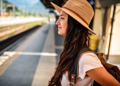 Eine Frau steht am Bahnhof, um ihre Staedtereise mit dem Zug zu beginnen, und freut sich auf die bevorstehende Entdeckung neuer Staedte. | © Gettyimages.com/MStudioImages