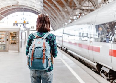 Frau mit Rucksack beobachtet einen Zug am Bahnhof | © GettyImages.com/frantic00