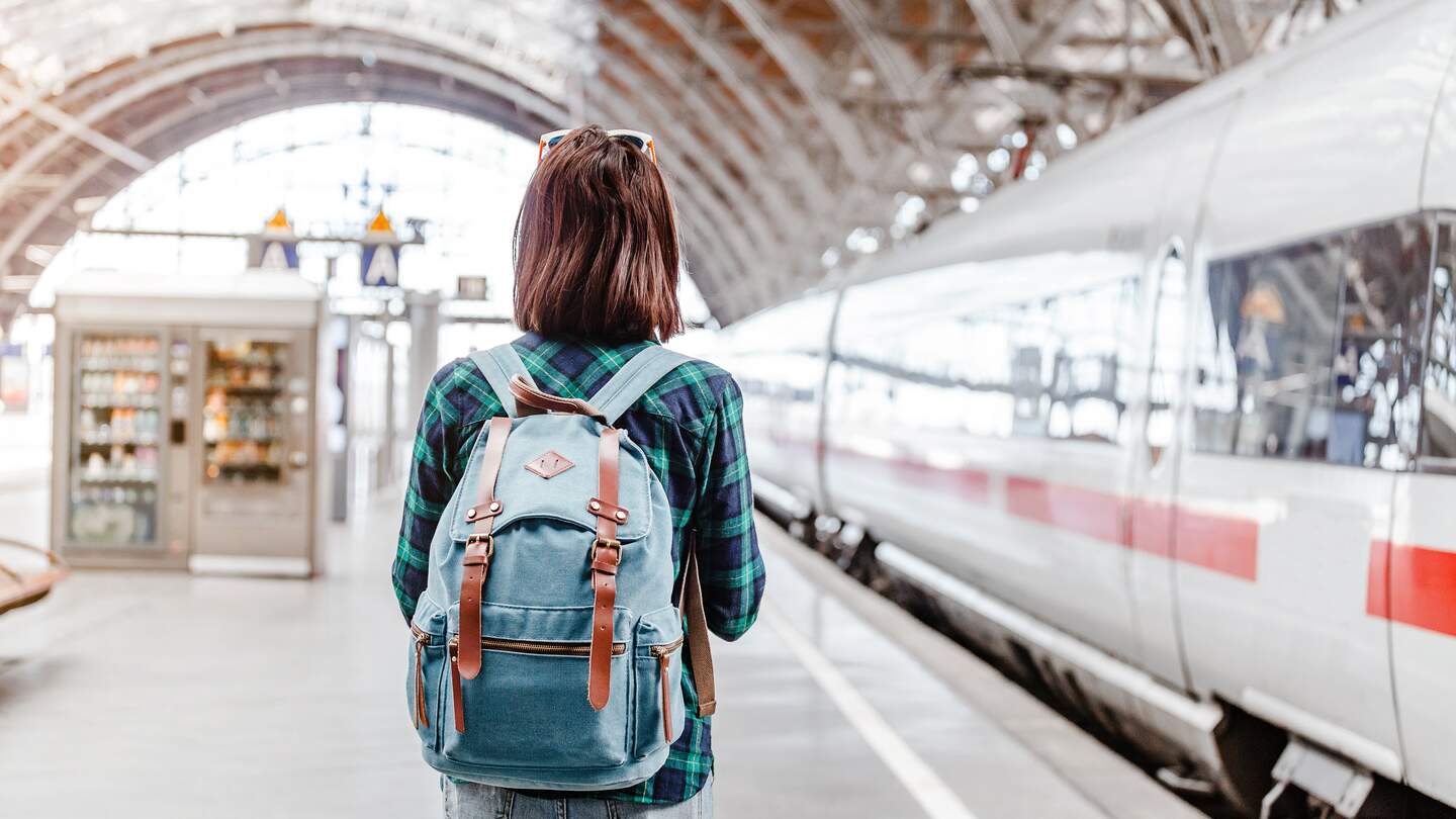 Frau mit Rucksack beobachtet einen Zug am Bahnhof | © GettyImages.com/frantic00