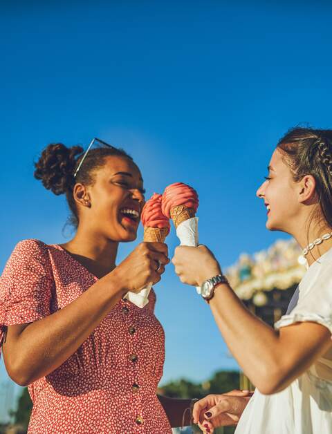 Zwei fröhliche, junge Frauen haben einen spaßigen Tag in Paris, Eis essend auf dem Rummel | © Gettyimages.com/Charday Penn