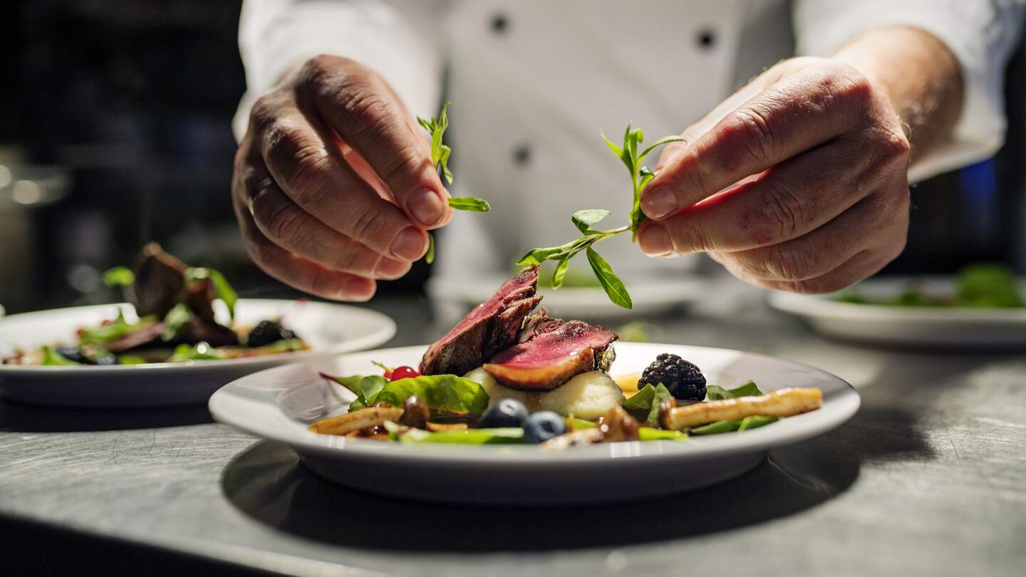 Koch dekoriert Essen. Das Gericht ist, gebratene rosa Entenbrust auf ein Bett aus Pastinakenpueree mit saisonalem Herbstgemuese und Beeren. | © Gettyimages.com/ClarkandCompany