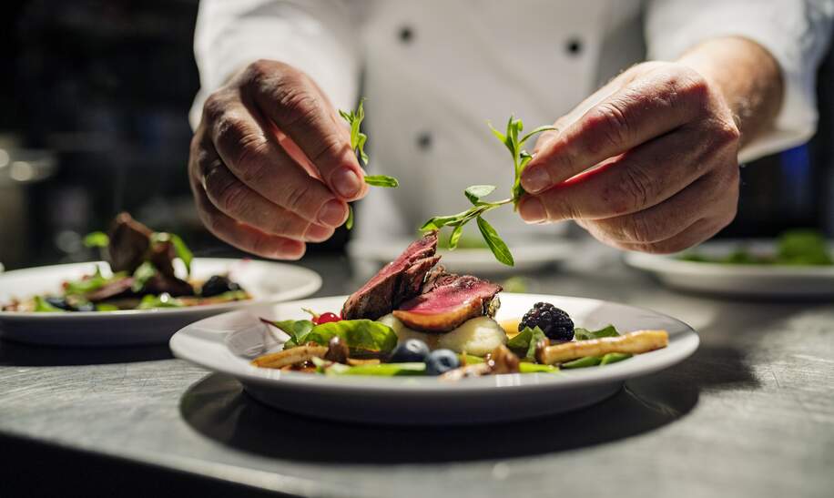 Koch dekoriert Essen. Das Gericht ist, gebratene rosa Entenbrust auf ein Bett aus Pastinakenpueree mit saisonalem Herbstgemuese und Beeren. | © Gettyimages.com/ClarkandCompany